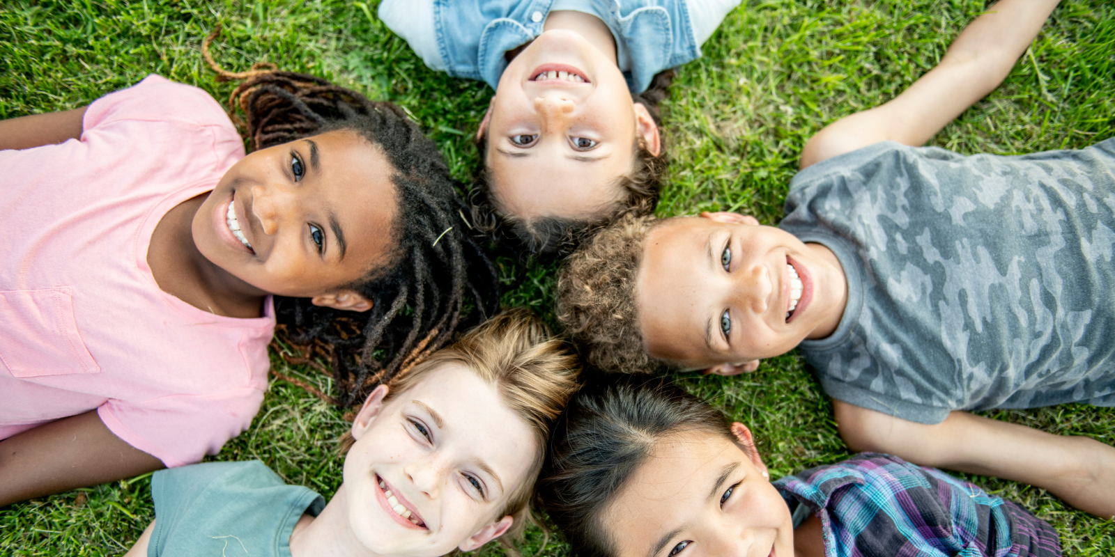 A circle of happy, diverse children lying in the grass looking up